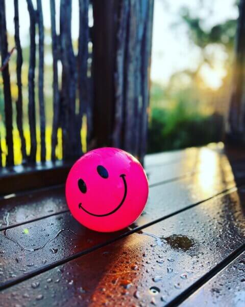 close up of a pink ball with a smiley face sitting on a wet deck
