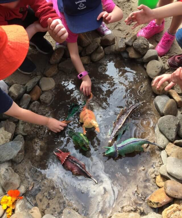 children playing with toy dinosaurs in puddle of water